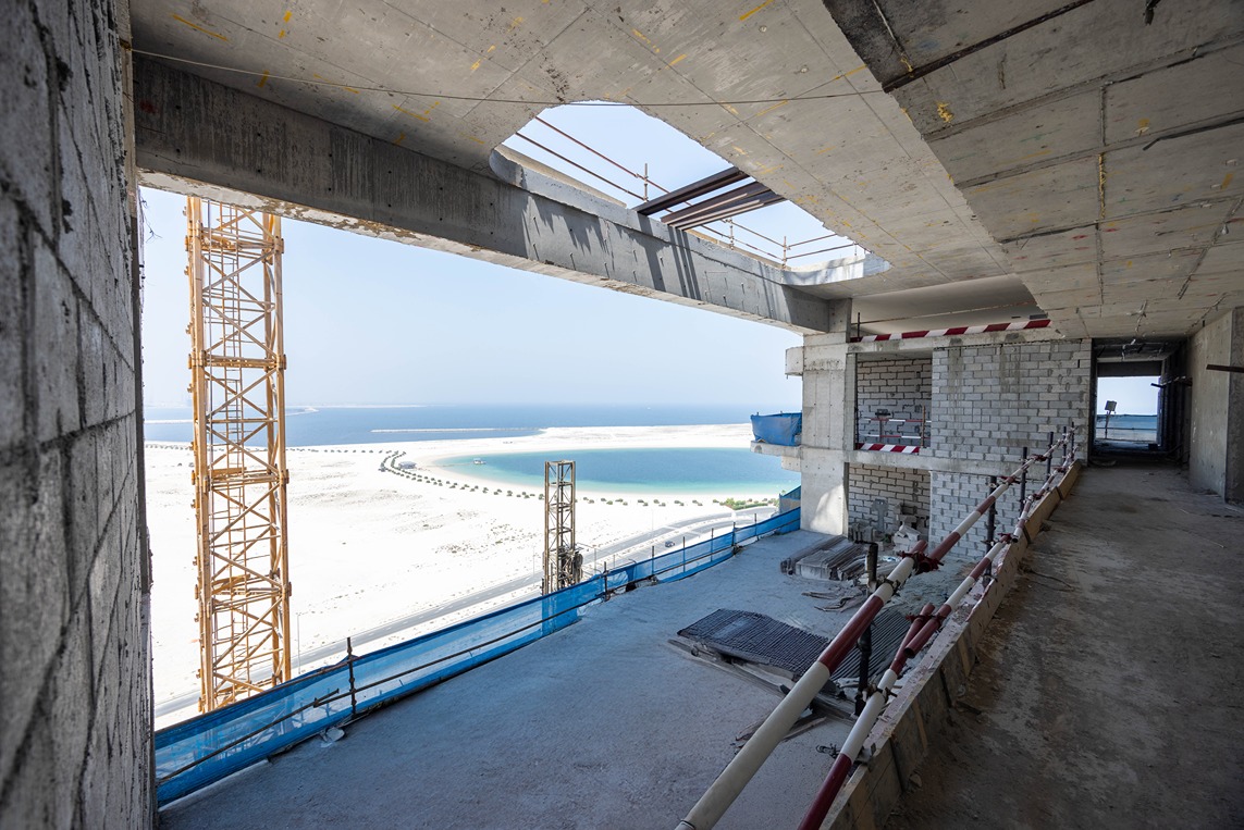 Beach Walk Residence A construction site with unfinished concrete walls and scaffolding overlooking a scenic beach and sea.