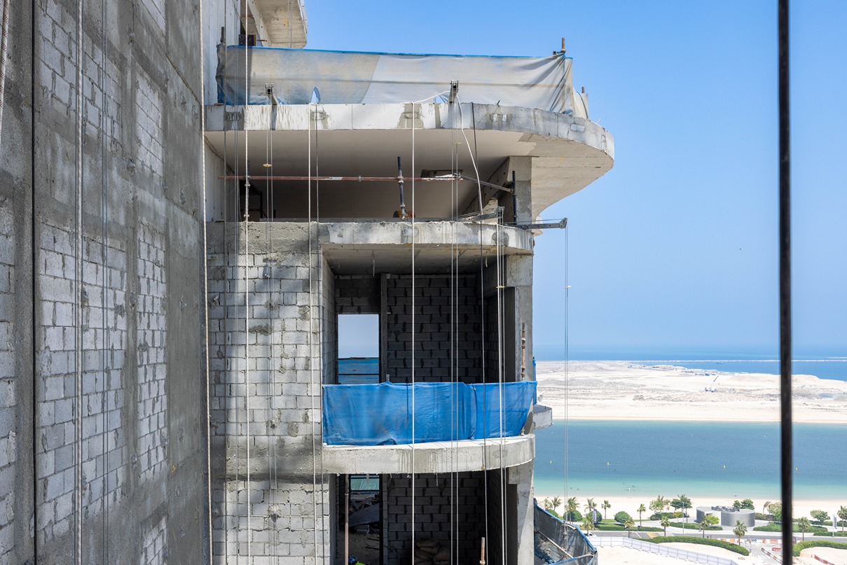 Beach Walk Residence Construction site of a building with unfinished walls and blue safety barriers, overlooking a beach and water.
