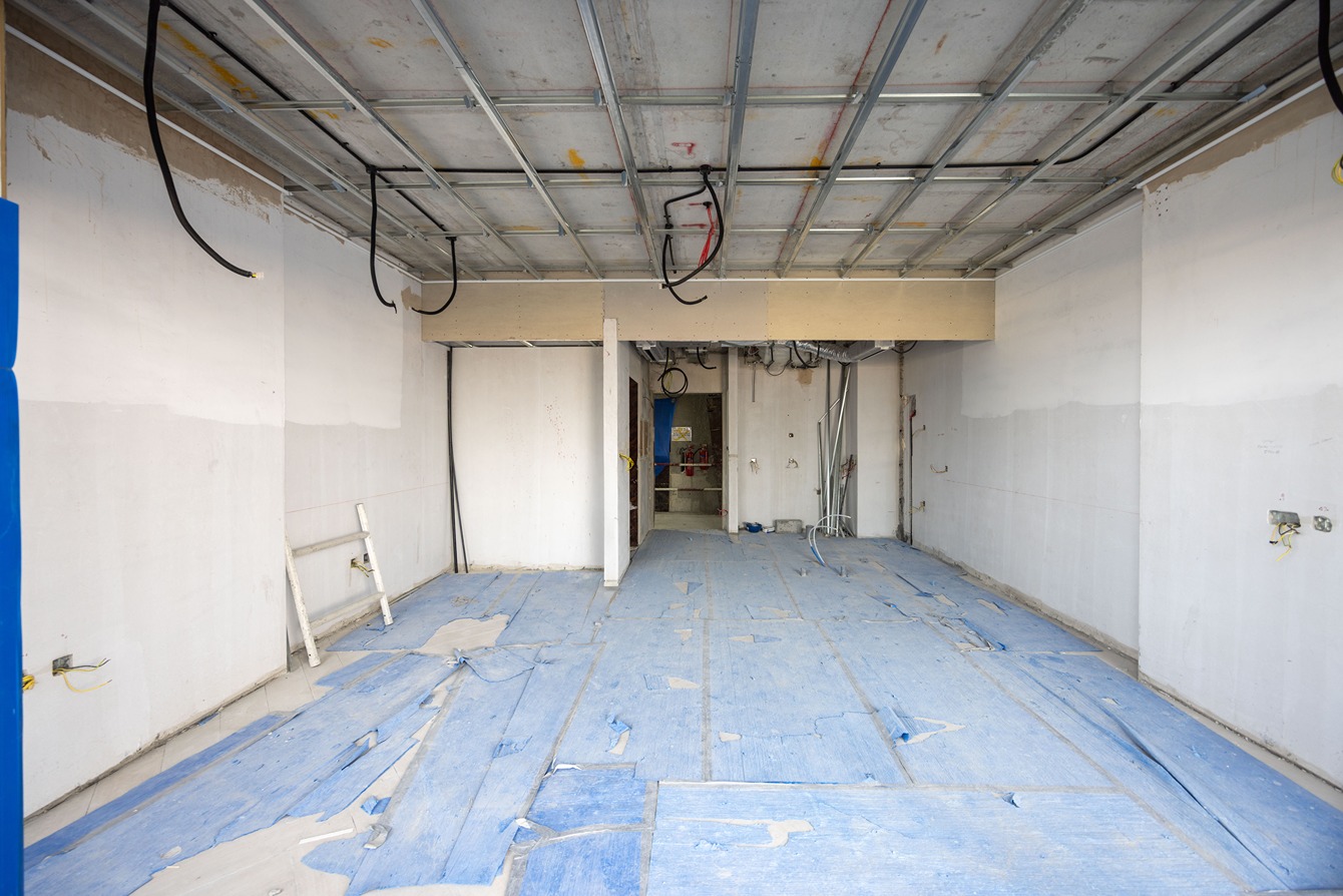Beach Walk Residence Empty room under construction with blue protective covering on the floor and exposed wiring on the ceiling.