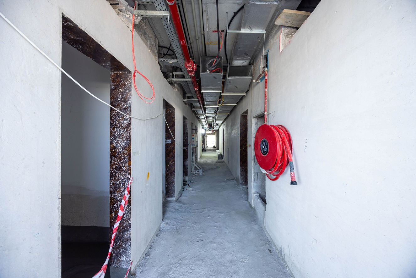 Beach Walk Residence An unfinished hallway with exposed pipes, open doorways, and scattered construction materials.