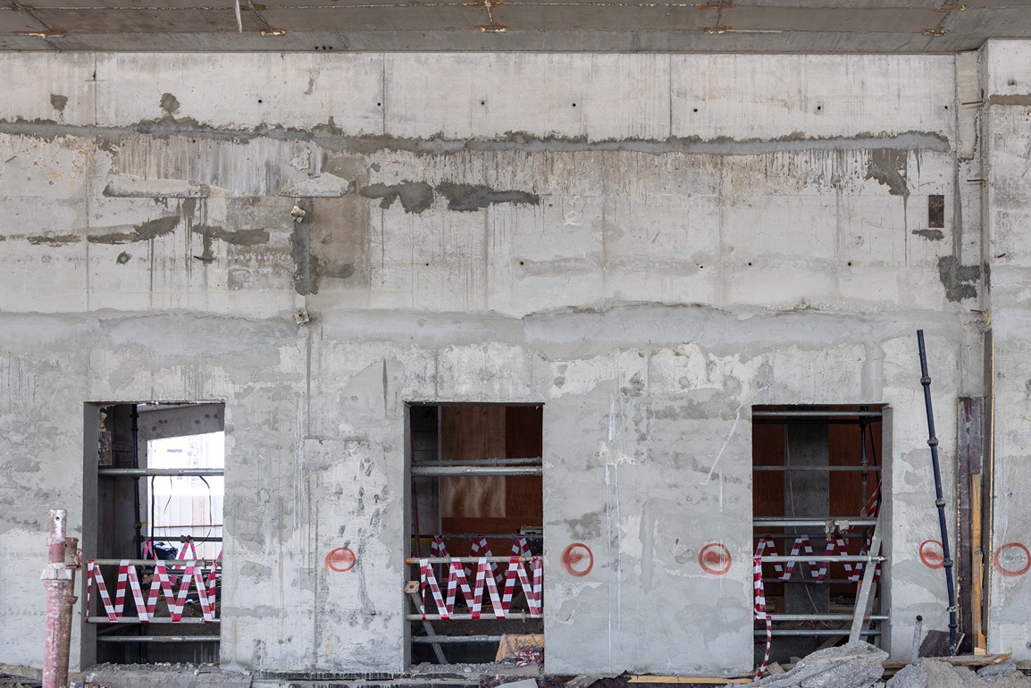 Beach Walk Iii By Imtiaz Concrete wall with three window openings, scaffolding inside, and red caution tape across the bottom.