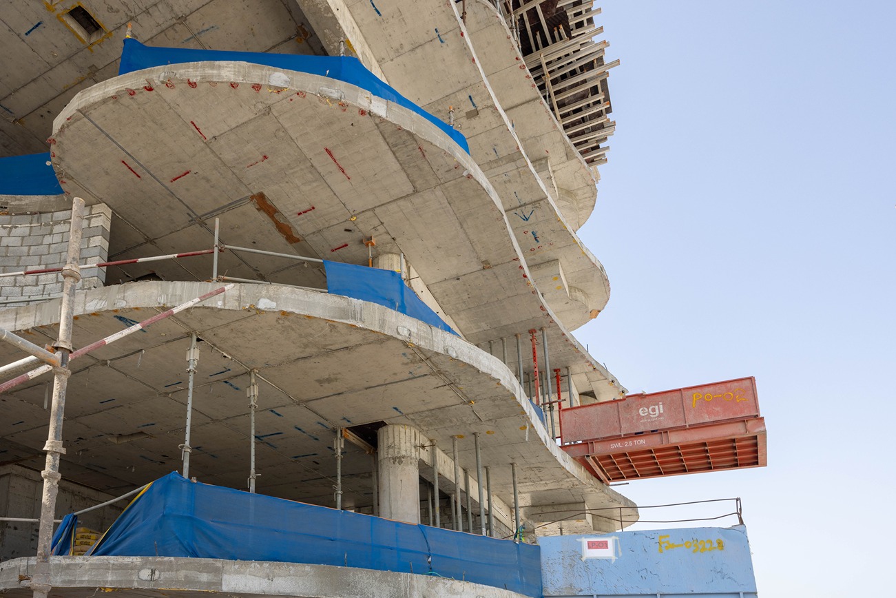 Beach Walk Iii By Imtiaz Modern building under construction featuring curved concrete floors, scaffolding, and protective blue sheeting.