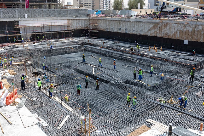 Cove Edition I By Imtiaz 1 Construction site with workers in safety gear, installing rebar in a large concrete foundation.