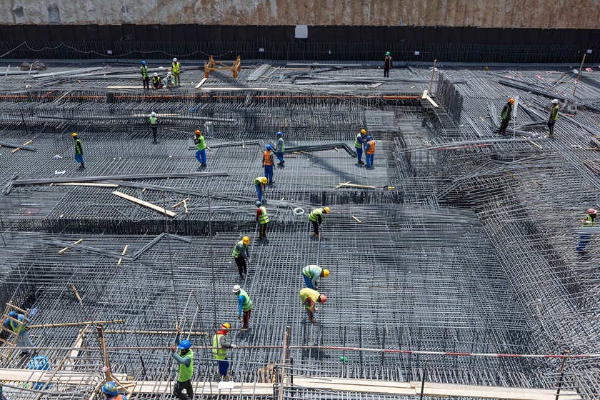 Cove Edition I By Imtiaz 1 Construction workers are laying rebar on a large site under a bright sky, focused on structural work.