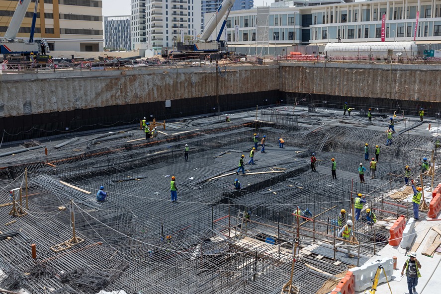 Cove Edition I By Imtiaz 1 Construction site with workers in safety gear managing reinforcement bars in a deep foundation excavation.