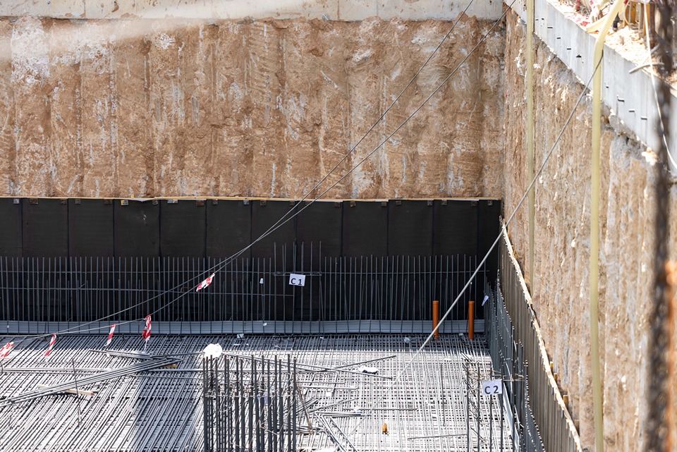 Cove Edition I By Imtiaz 1 A construction site showing a deep foundation with exposed soil and rebar grids for structural reinforcement.