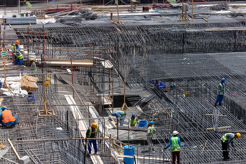 Cove Edition I By Imtiaz 1 Construction site with multiple workers in safety gear managing rebar and scaffolding in a busy environment.