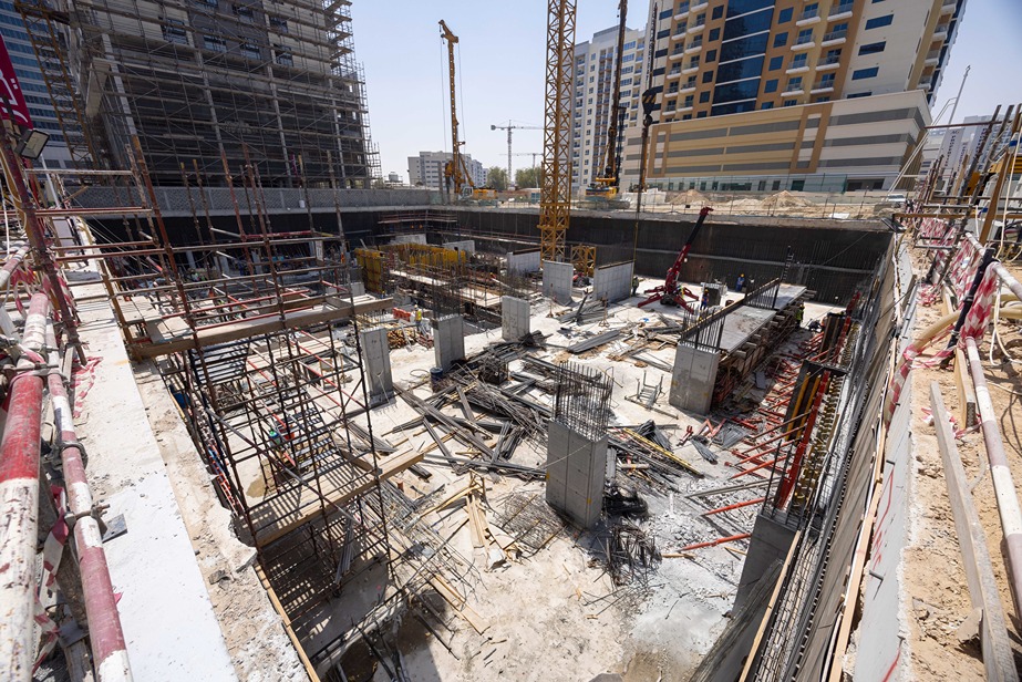 Cove Edition I By Imtiaz 1 A construction site with scaffolding, cranes, and concrete structures under development in an urban area.