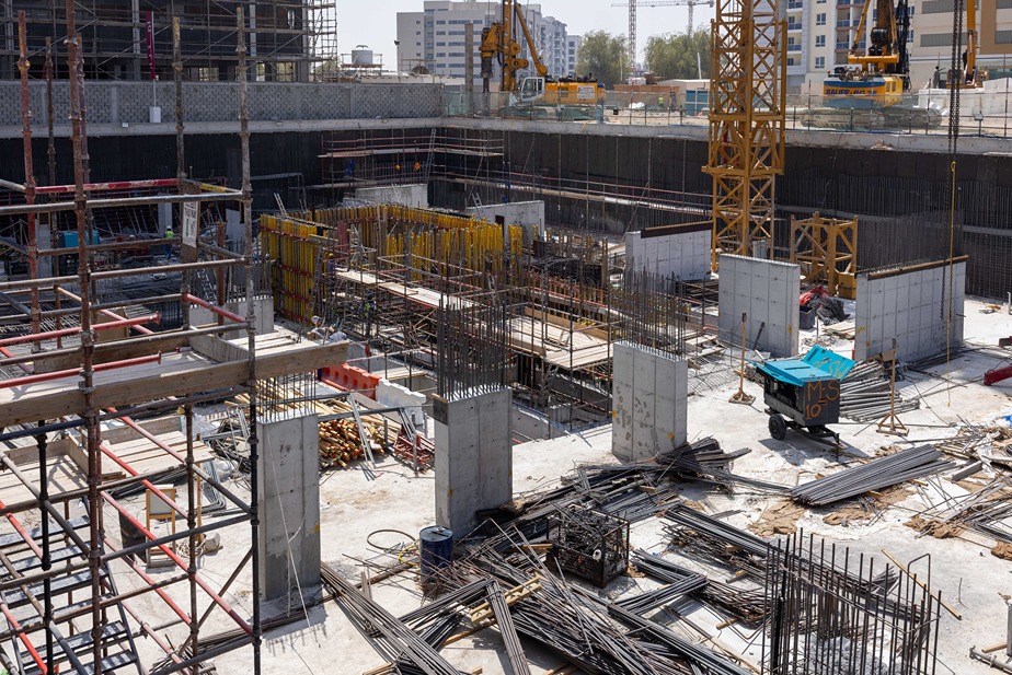 Cove Edition I By Imtiaz 1 Construction site featuring rebar, scaffolding, concrete forms, and machinery in a large excavation area.