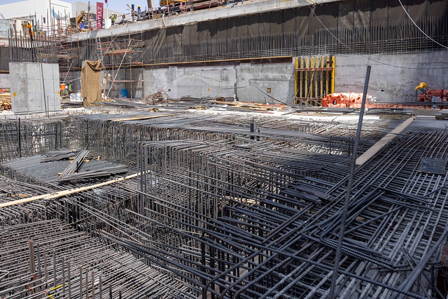 Cove Edition I By Imtiaz 1 Construction site featuring a grid of steel rebar, concrete walls, and scaffolding in the background.