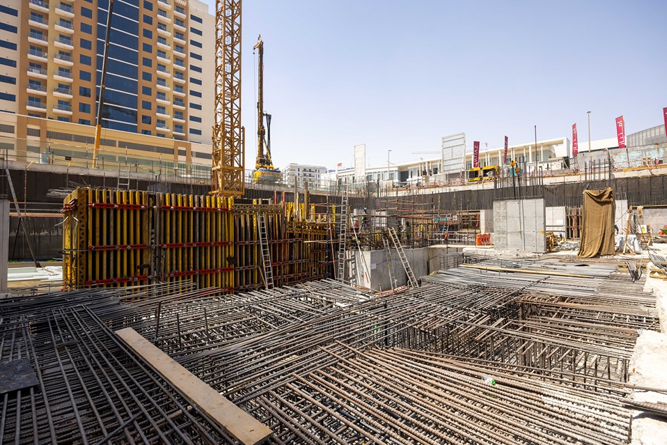 Cove Edition I By Imtiaz 1 A construction site with steel rebar and wooden forms, surrounded by cranes and buildings under development.