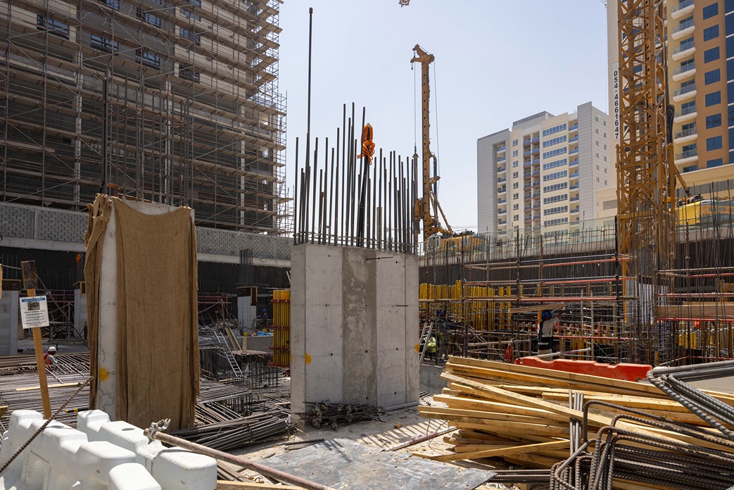 Cove Edition I By Imtiaz 1 Construction site with scaffolding, concrete pillars, steel rebar, and workers near buildings in progress.