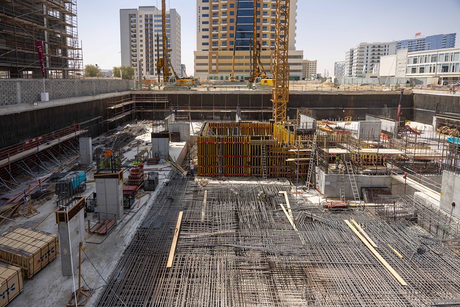Cove Edition I By Imtiaz 1 A construction site featuring cranes, concrete structures, and steel reinforcement bars in a city setting.