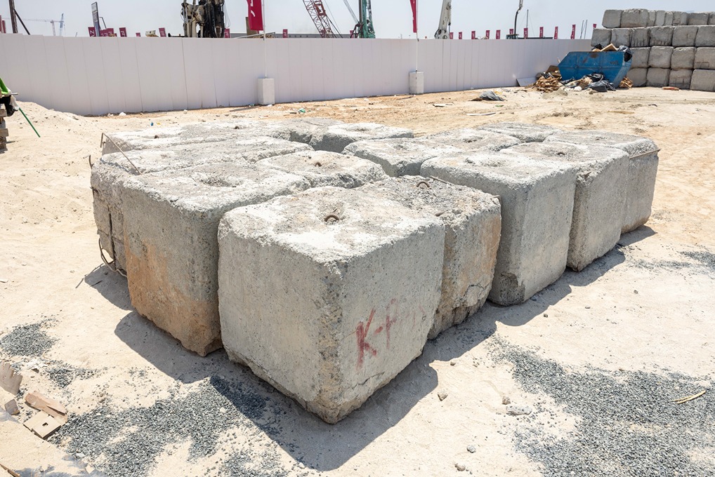Cotier House 2 By Imtiaz A stack of large concrete blocks on a construction site with machinery and a fence in the background.
