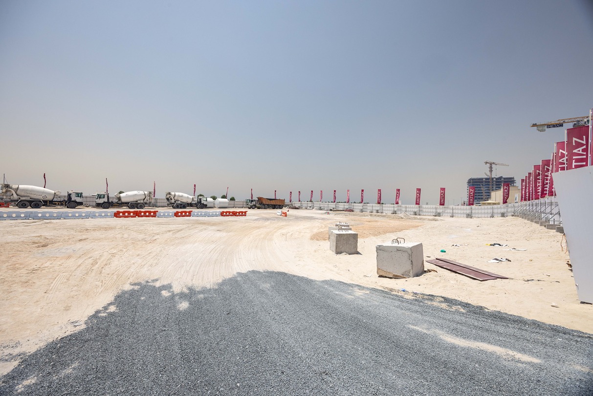 Cotier House 2 By Imtiaz Construction site with gravel, concrete mixers, safety barriers, and banners under a clear blue sky.