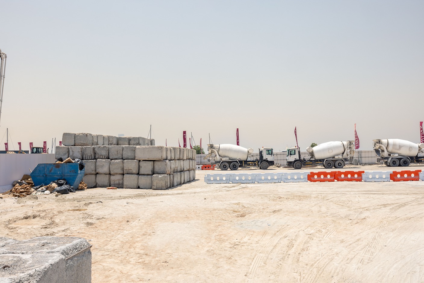 Cotier House 2 By Imtiaz A construction site featuring stacked concrete blocks, cement mixers, and barricades on a sandy surface under clear skies.