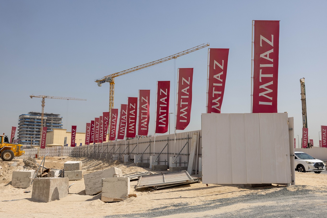 Cotier House 2 By Imtiaz Construction site featuring several "IMTIAZ" banners, cranes, machinery, and scattered building materials on sandy ground.