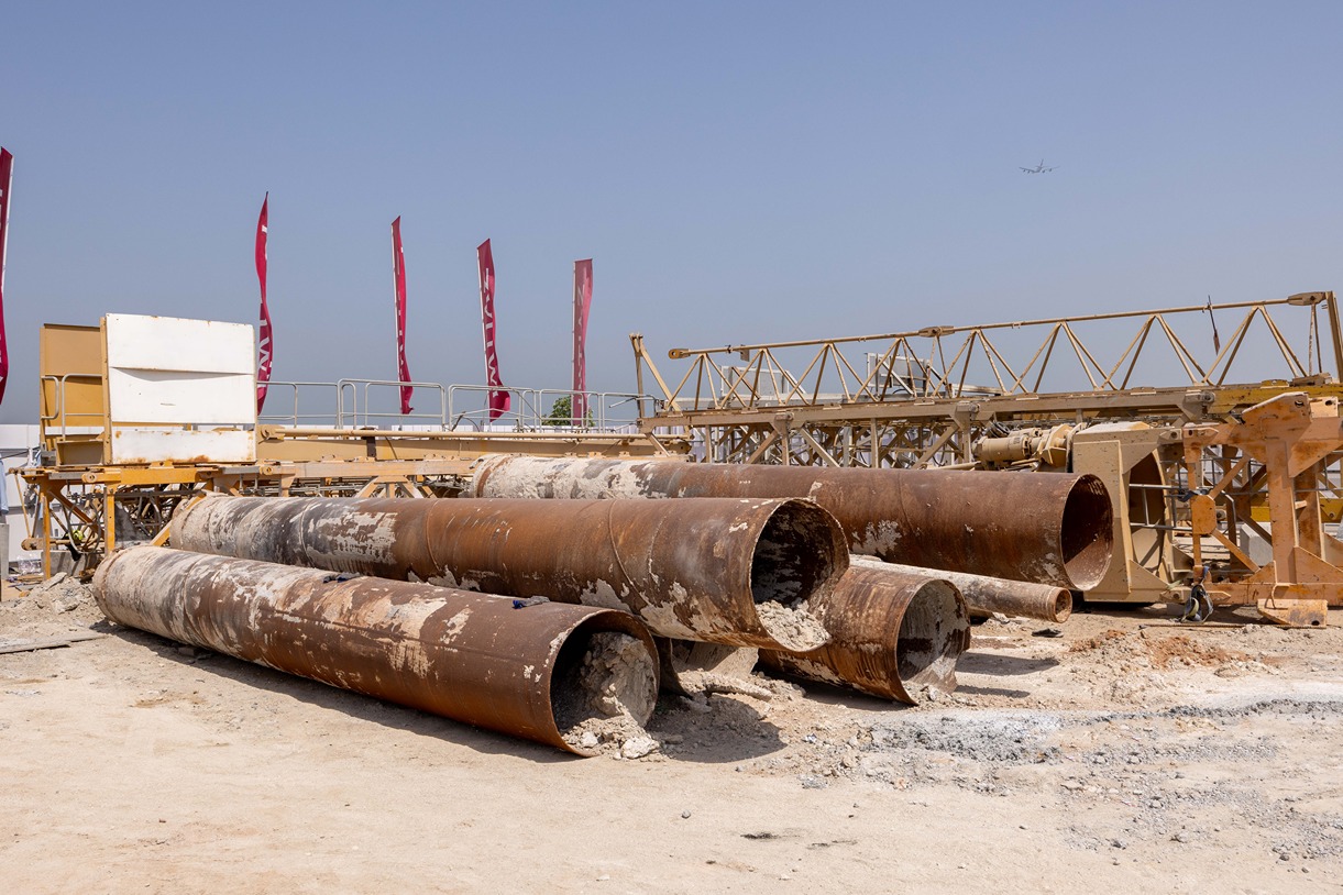Cotier House 2 By Imtiaz Construction site featuring large rusty pipes, machinery, and flags against a clear blue sky.