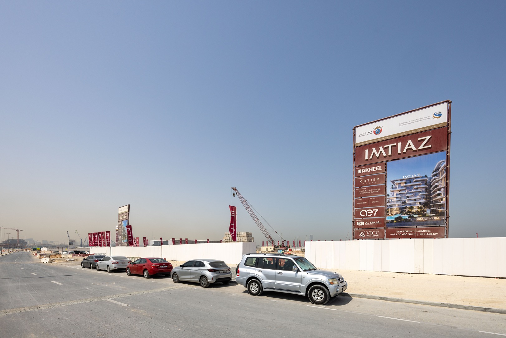 Cotier House 2 By Imtiaz Construction site with a large sign for "Imtiaz" and several parked cars along the road under a clear blue sky.