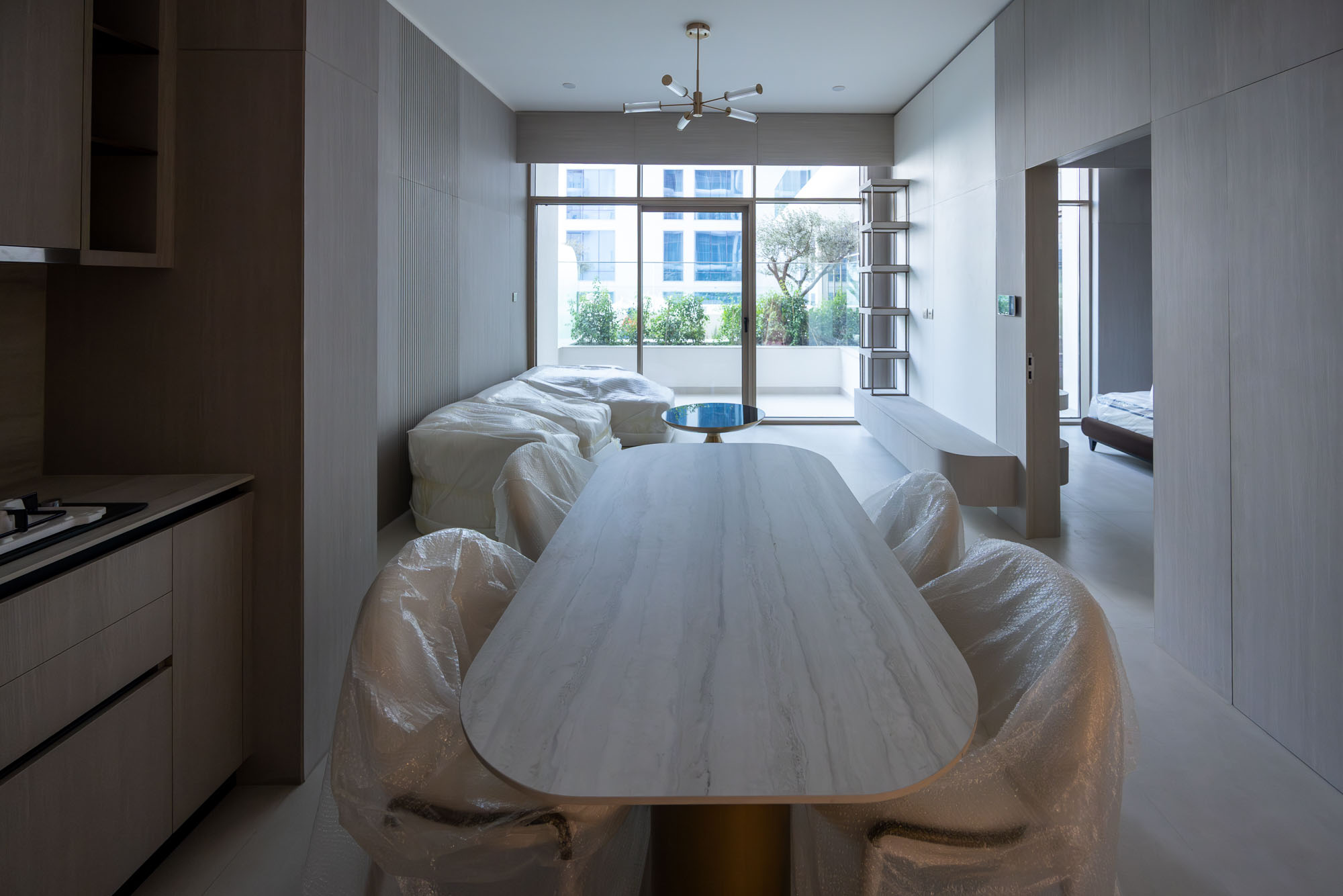 Pearl House By Imtiaz A modern, minimalistic dining area featuring a long table, plastic-covered chairs, and large windows.