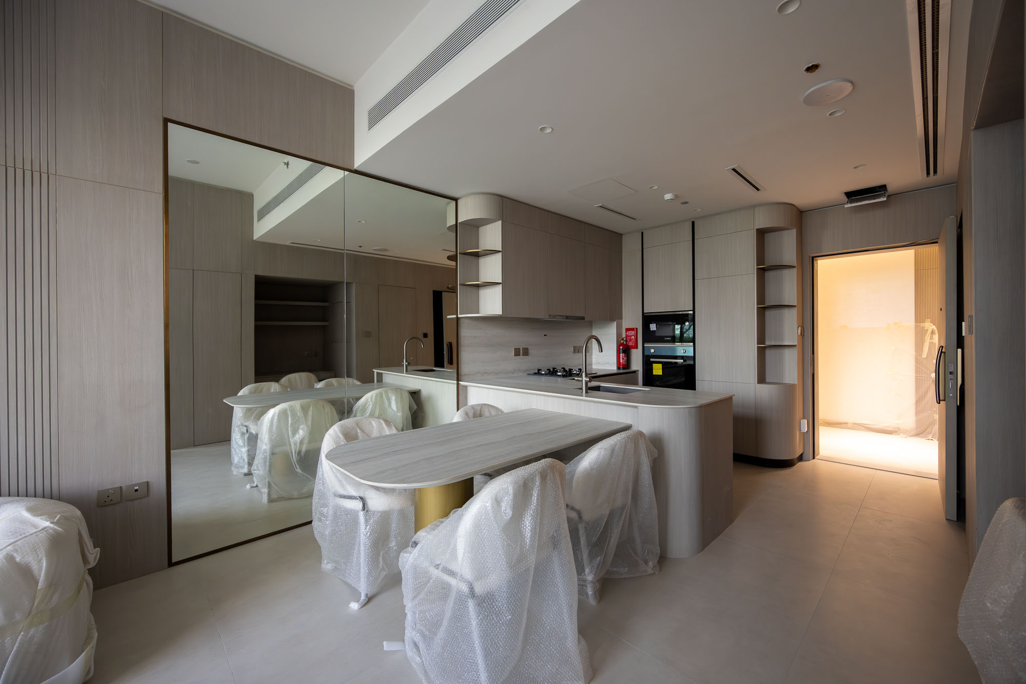 Pearl House By Imtiaz A modern kitchen with mirrored cabinets, a circular dining table, and chairs covered in protective plastic.