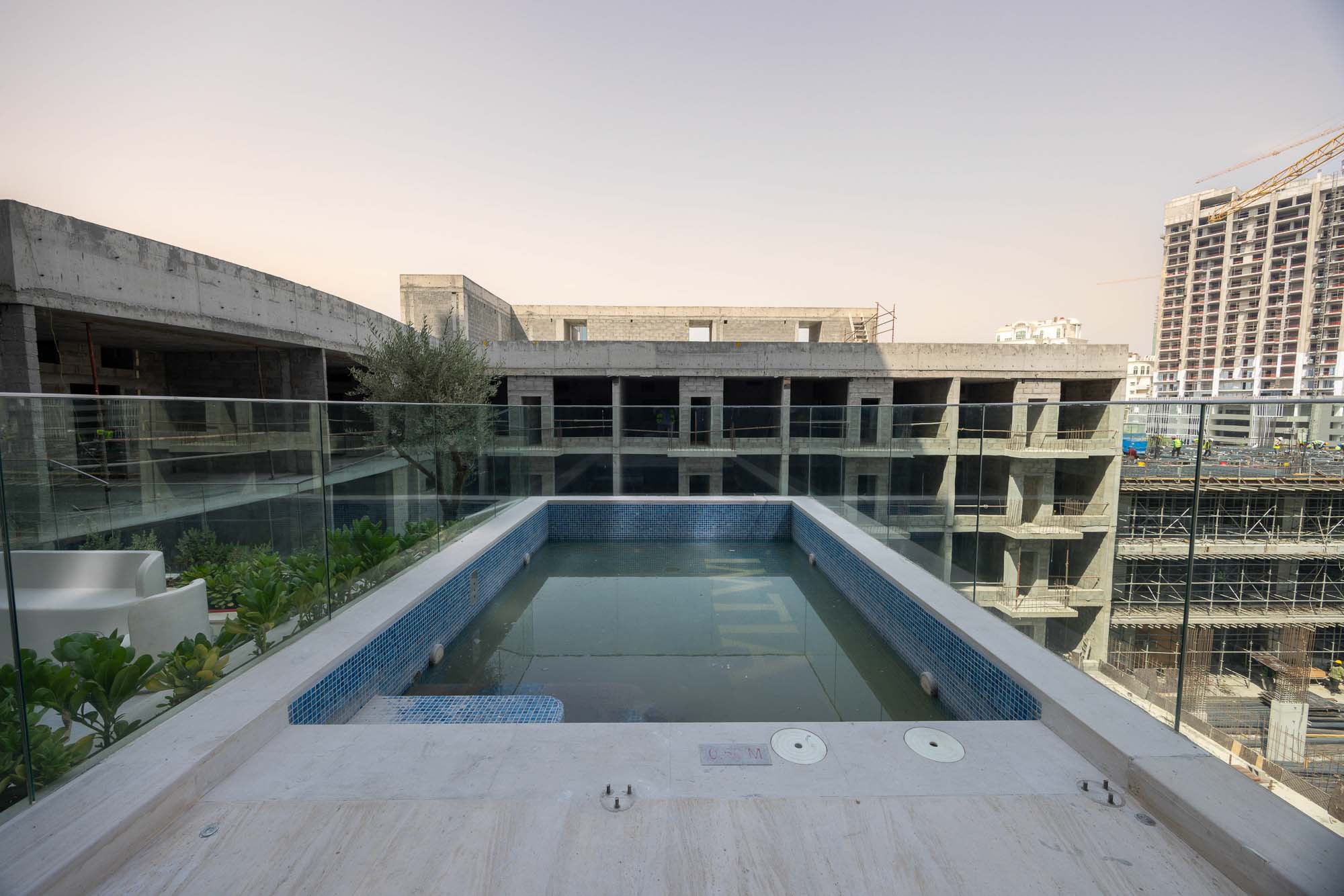 Pearl House By Imtiaz A rooftop view featuring a small pool surrounded by greenery, overlooking a construction site and buildings.