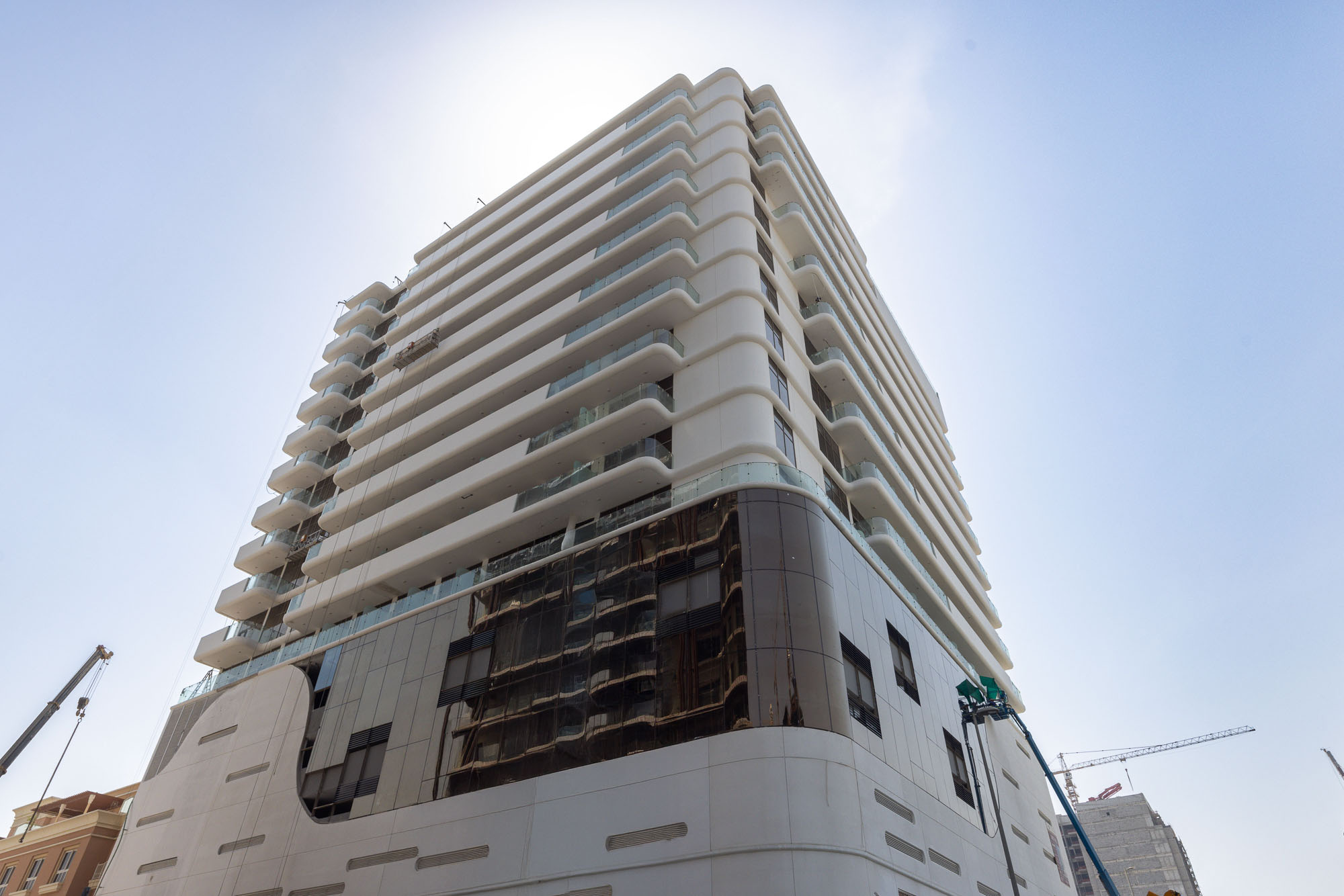 Pearl House By Imtiaz A modern multi-story building under construction, featuring balconies and glass facades, with cranes nearby.