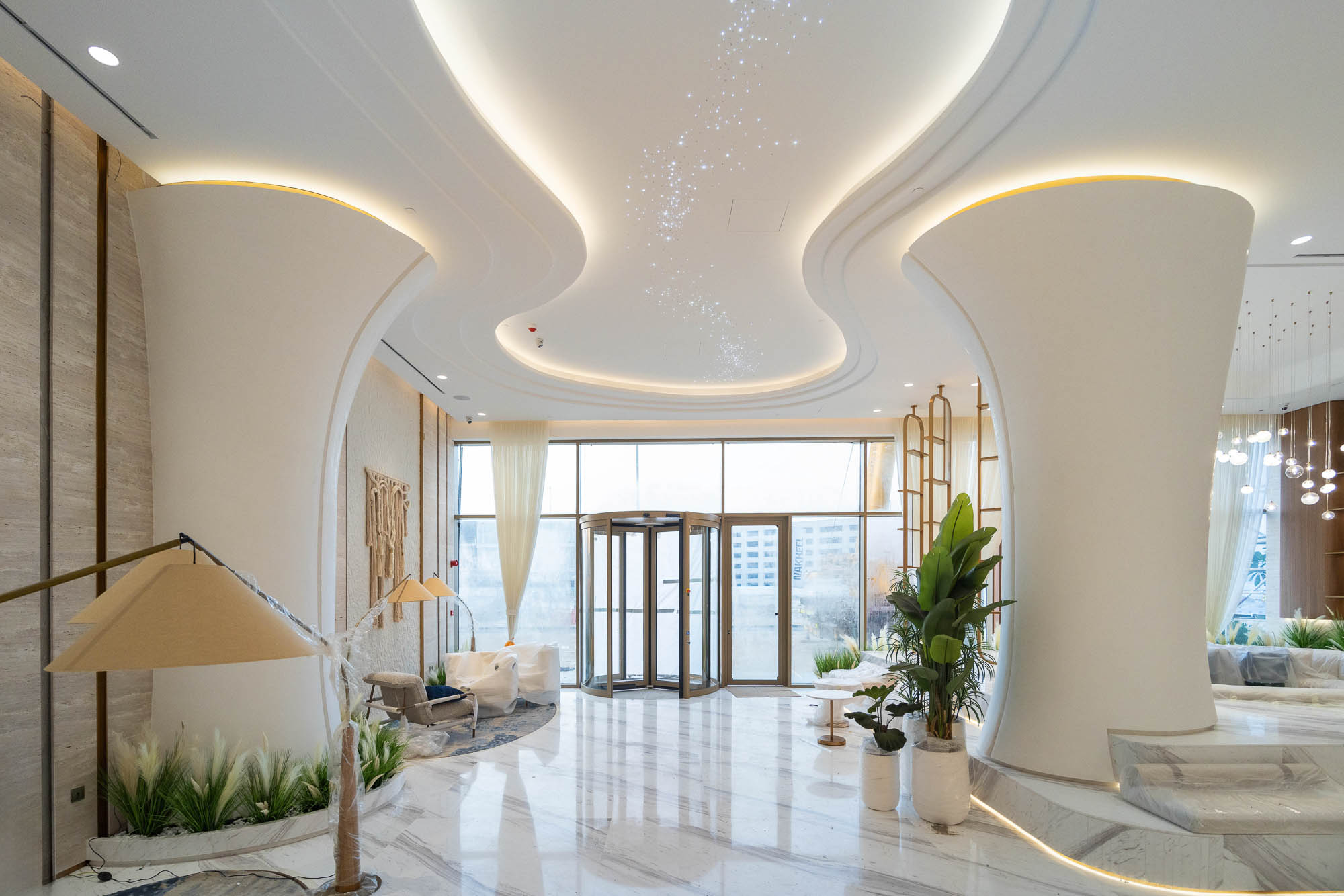 Beach Walk Residence A modern lobby featuring elegant decor, soft lighting, large windows, and lush greenery in a stylish design.