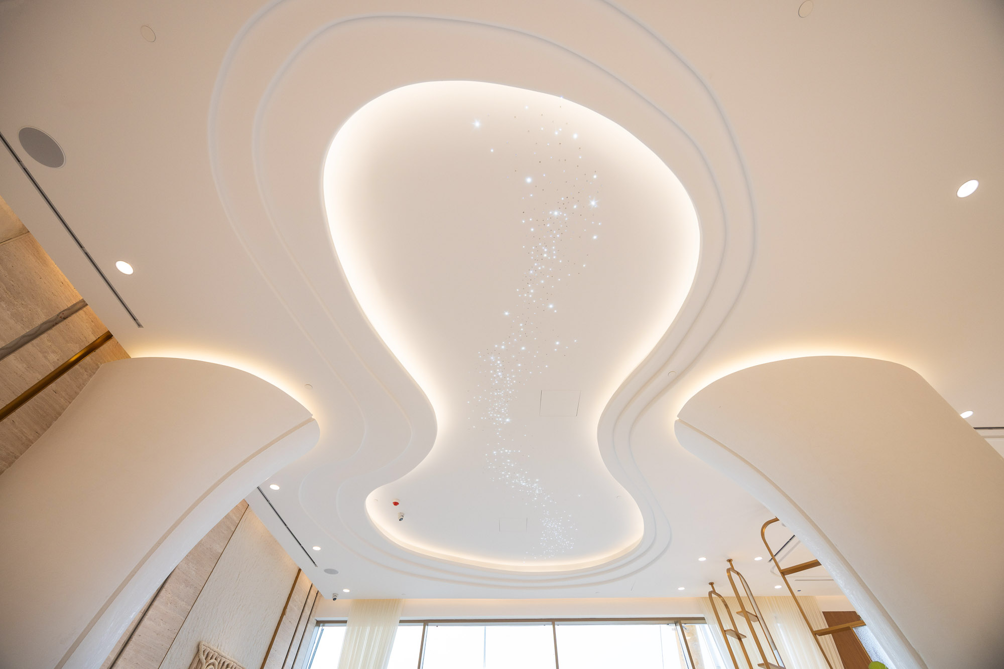 Beach Walk Residence A modern ceiling featuring smooth contours, soft lighting, and scattered star-like embellishments.