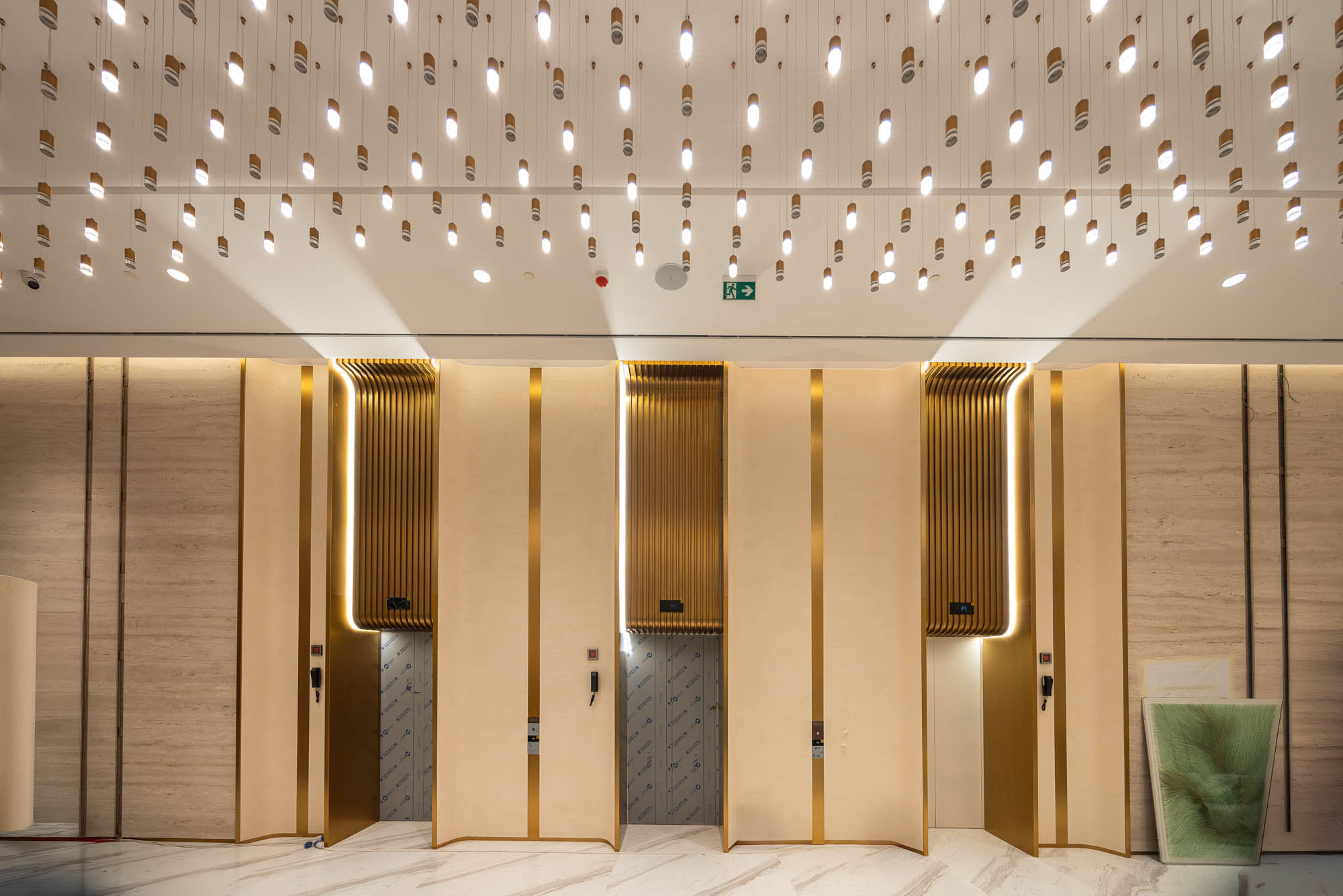 Beach Walk Residence Modern lobby with golden accents, sleek elevator doors, and unique hanging light fixtures illuminating the space.