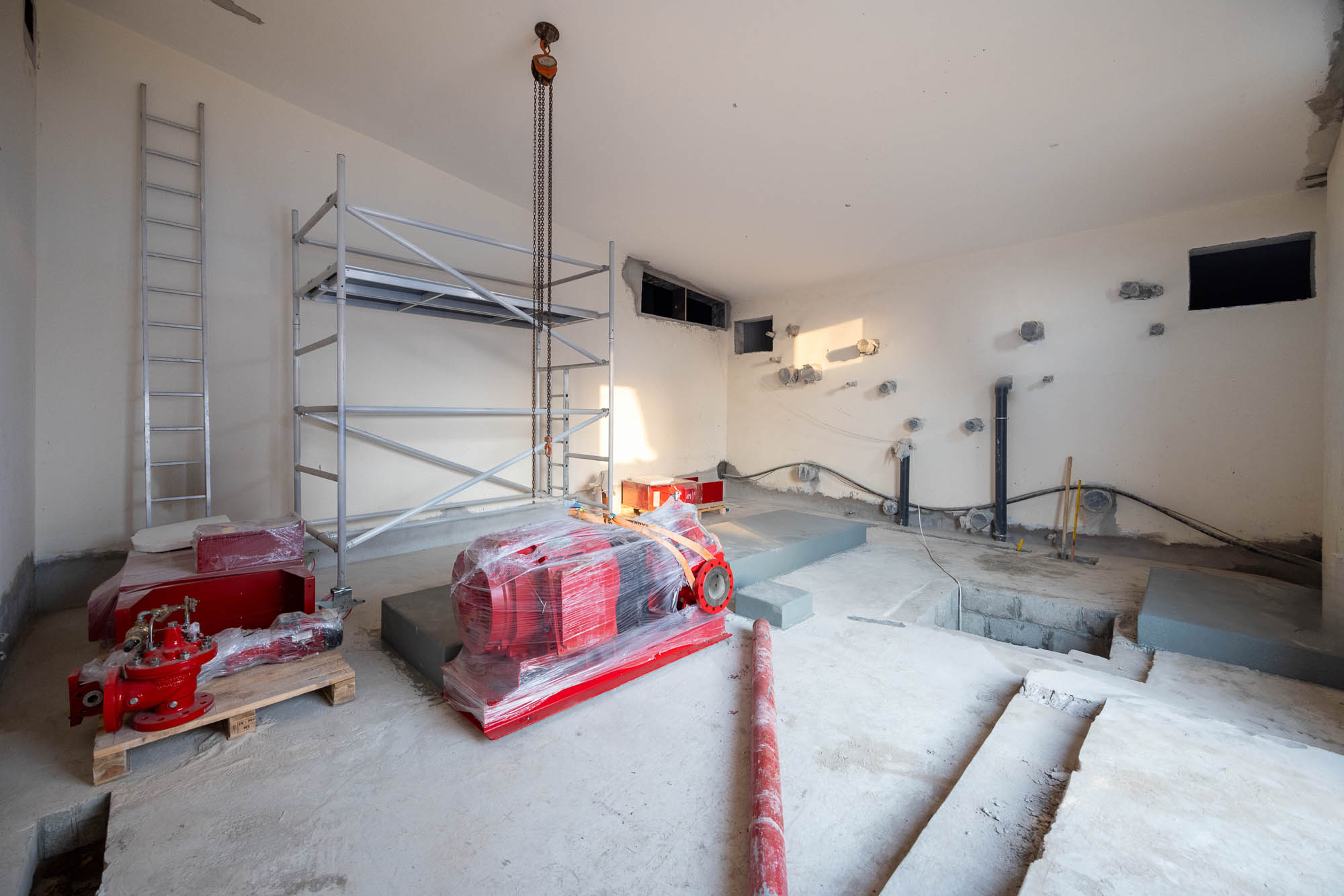 Beach Walk Residence An unfinished room with scaffolding, a ladder, and red machinery wrapped in plastic on a concrete floor.