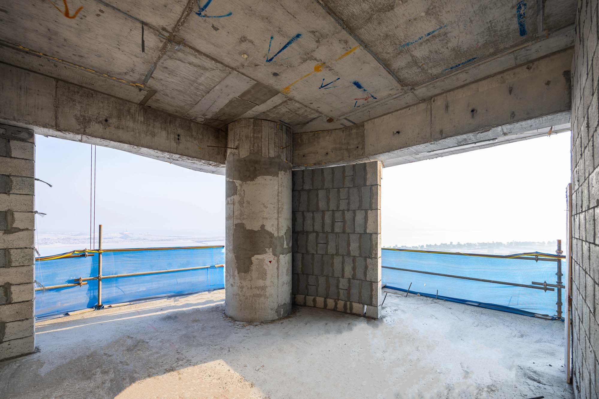 Beach Walk Iii By Imtiaz Interior view of an unfinished building with concrete pillars, block walls, and blue construction barriers outside.