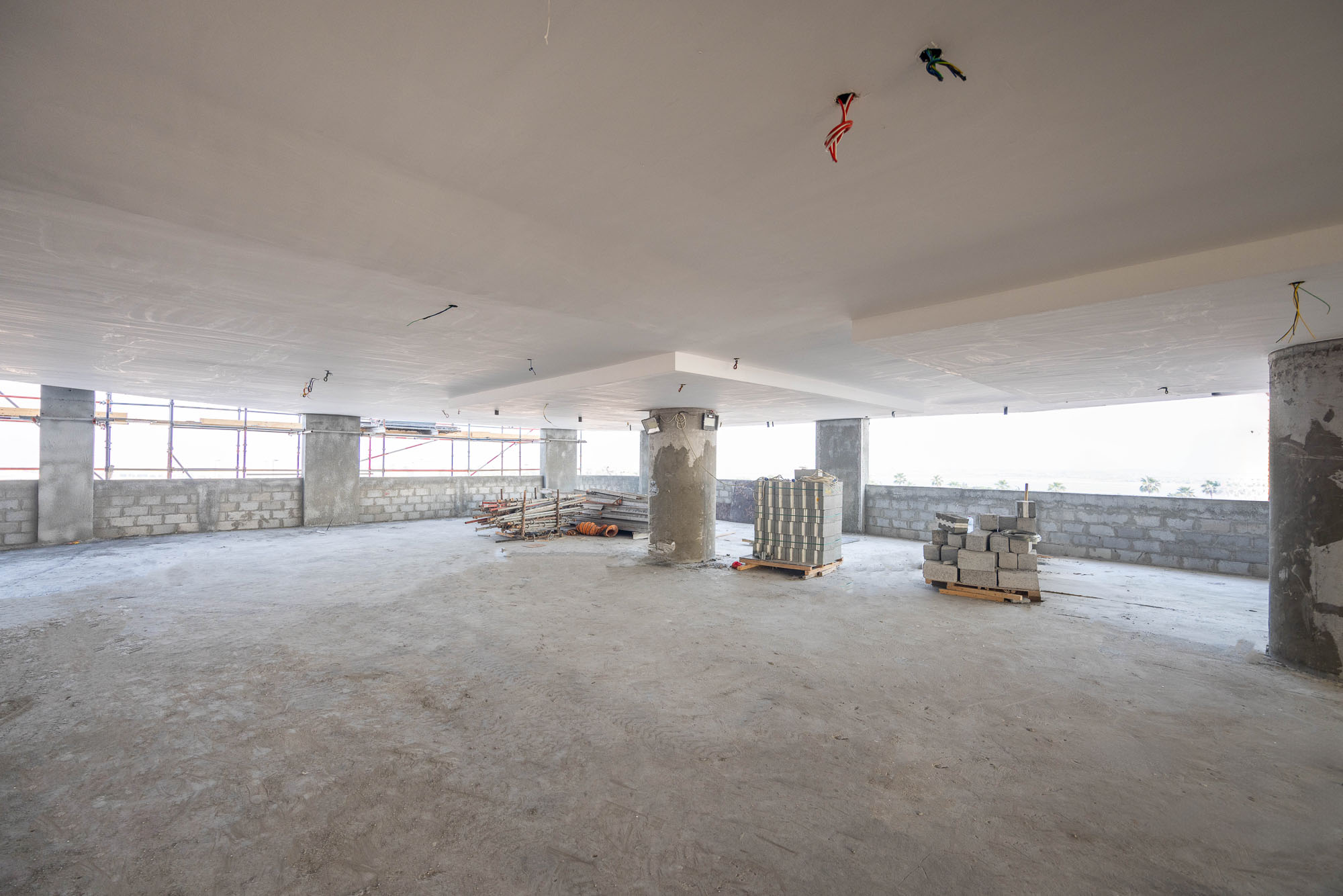 Beach Walk Iii By Imtiaz An empty construction site with exposed concrete pillars, stacks of building materials, and scaffolding visible through windows.