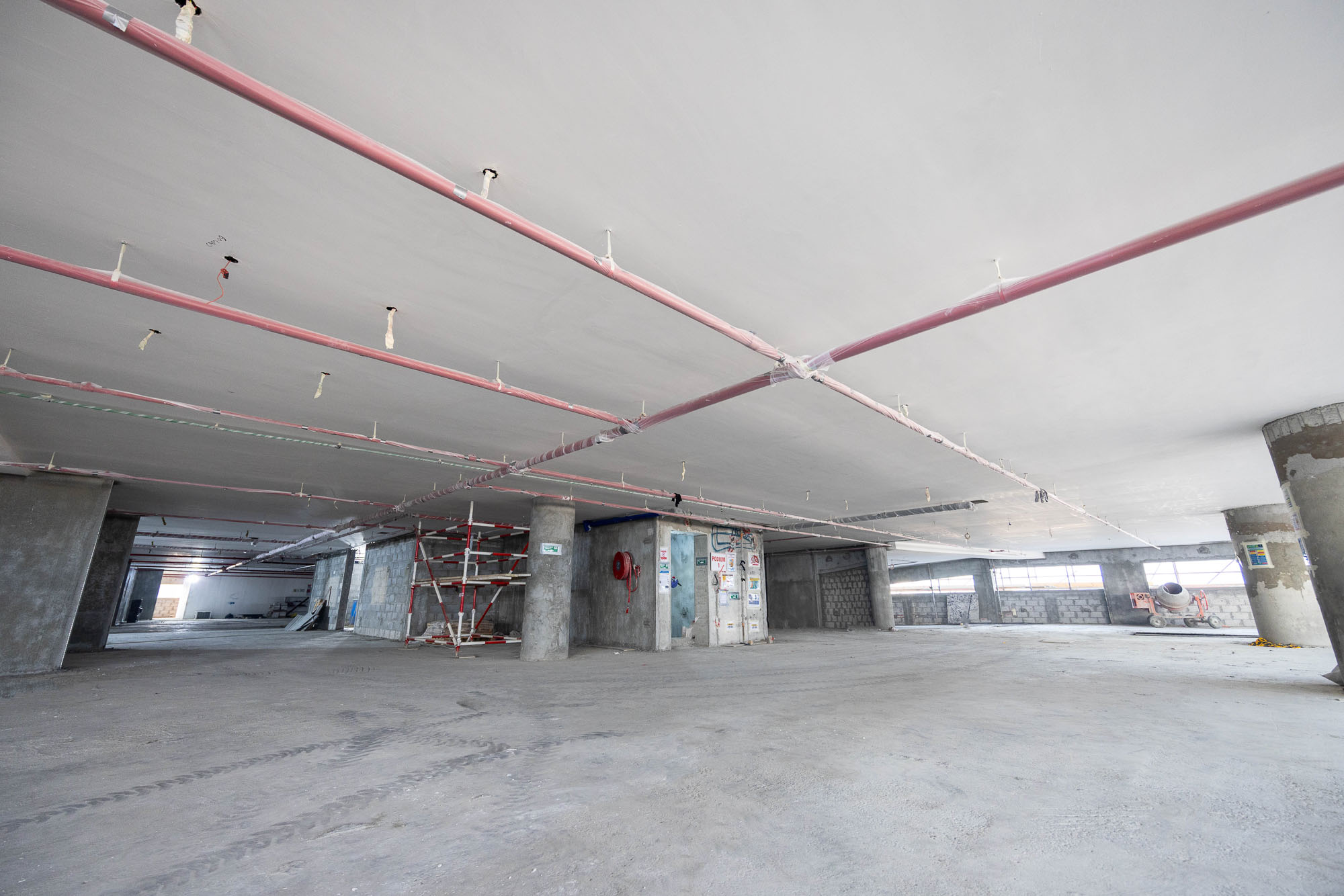 Beach Walk Iii By Imtiaz A spacious unfinished interior space with exposed ceilings, pipes, and scaffolding, featuring a bare concrete floor.