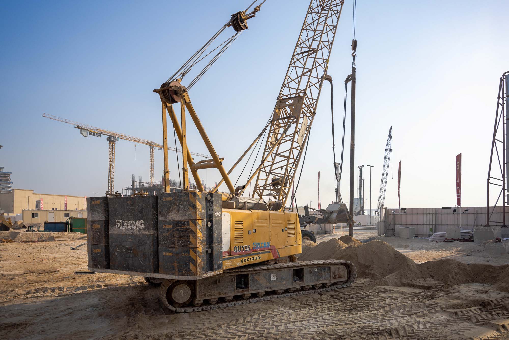 Cotier House 2 By Imtiaz A large yellow crane on a construction site with piles of dirt and other cranes in the background under a clear sky.