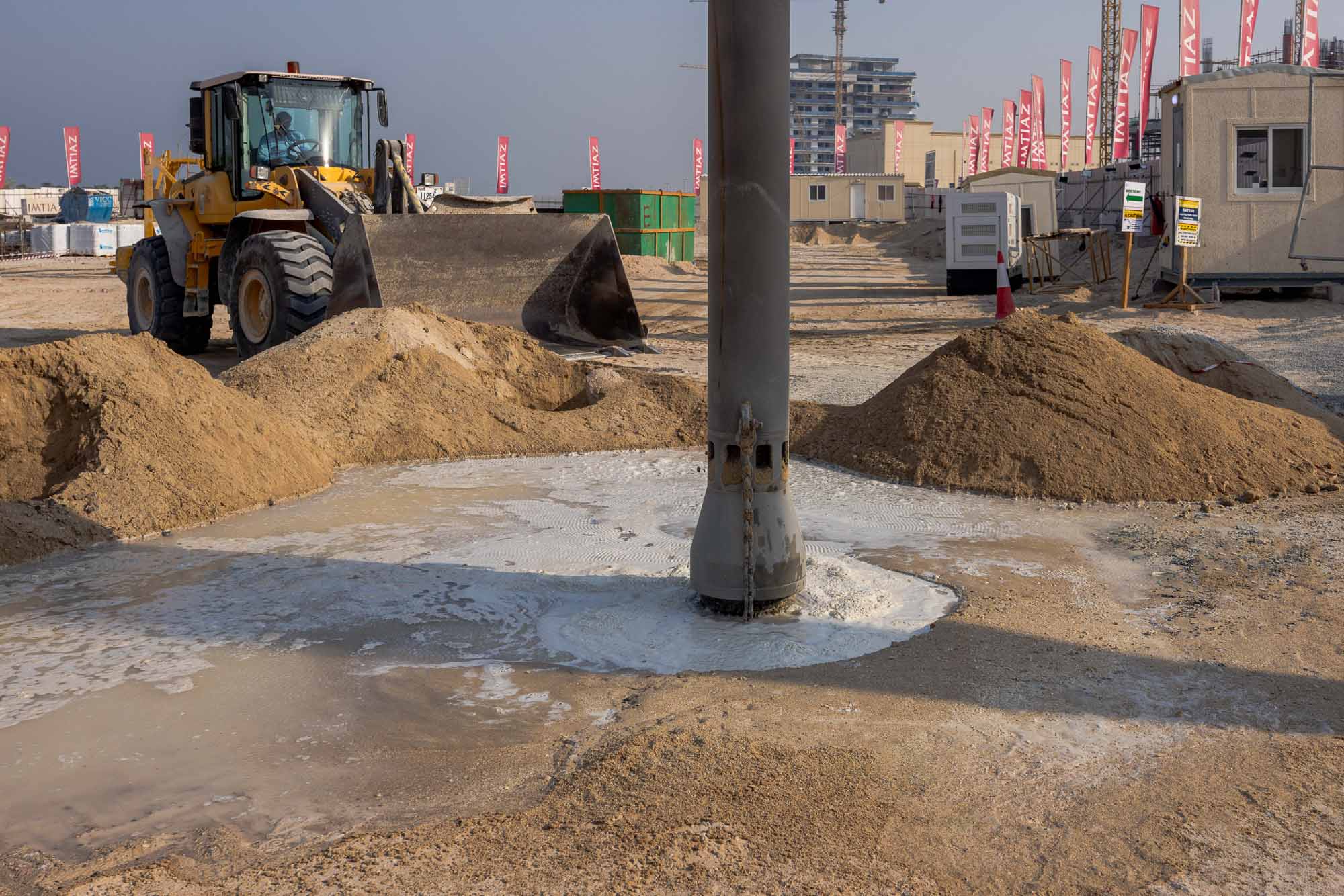 Cotier House 2 By Imtiaz A construction site featuring a loader, earth piles, and a water-filled area around a drilling post.