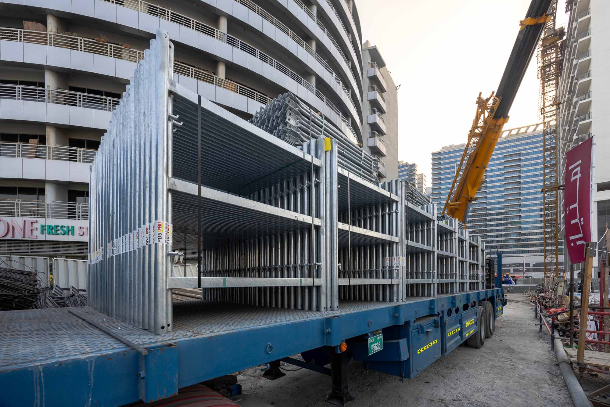 Cove Edition I By Imtiaz 1 A flatbed truck loaded with construction materials parked near a building site with cranes and surrounding structures.