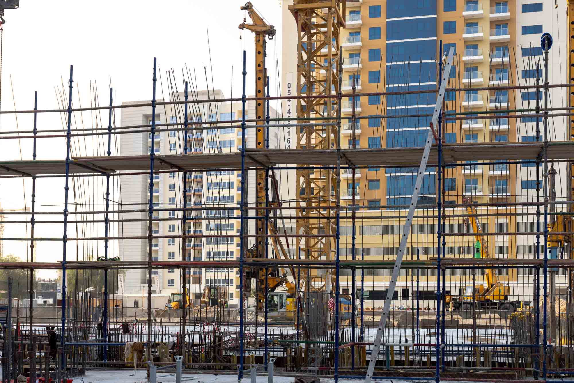 Cove Edition I By Imtiaz 1 Construction site featuring scaffolding and cranes, with a partially built multi-story building in the background.