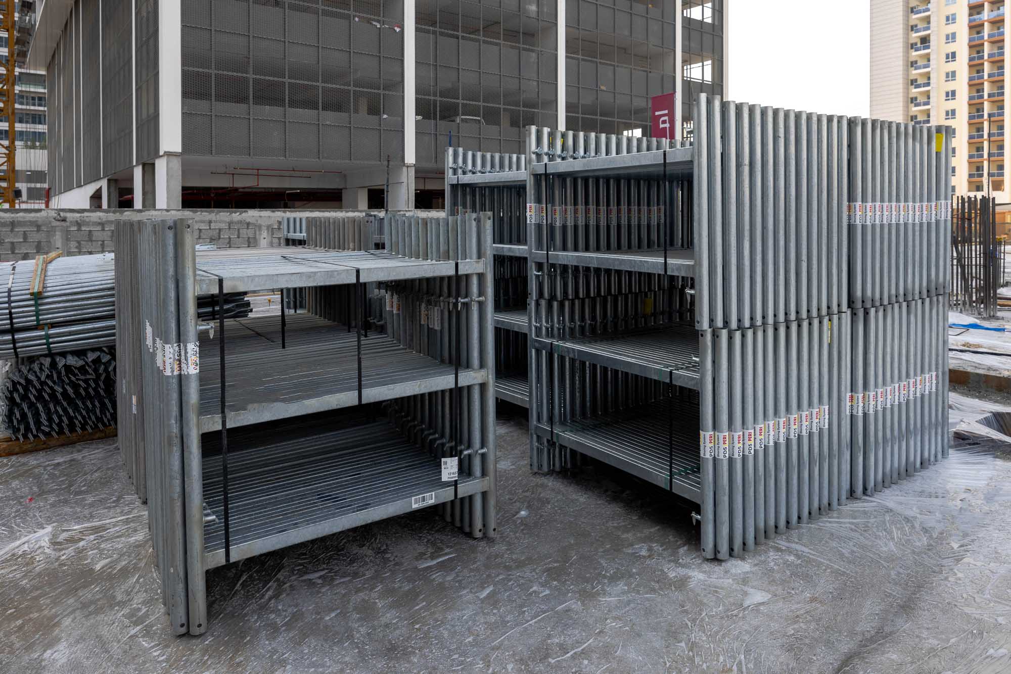 Cove Edition I By Imtiaz 1 Metal shelving units stacked on a construction site, surrounded by construction materials and equipment.