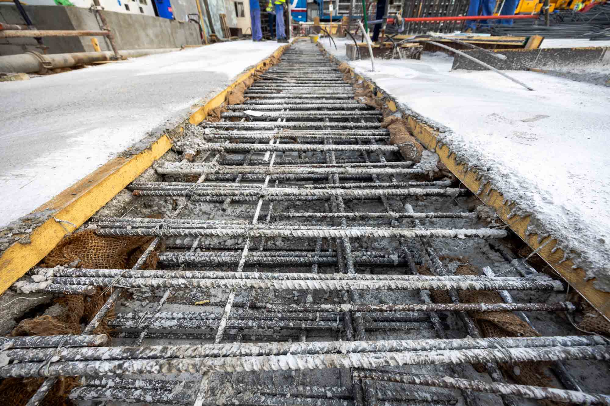 Cove Edition I By Imtiaz 1 A construction site showing rebar and fresh concrete on a pathway under construction, with tools and equipment nearby.