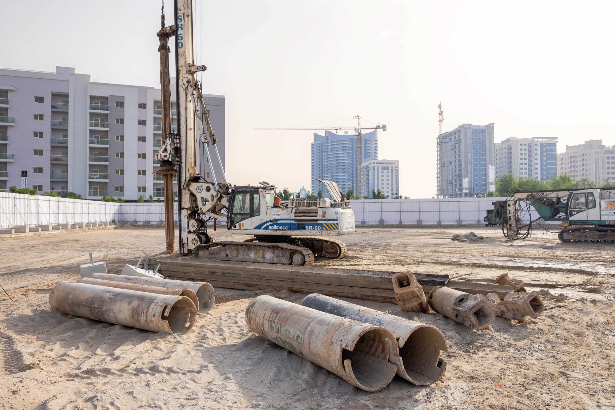 Cove Grand By Imtiaz Construction site featuring machinery, concrete pipes, and buildings in the background under a clear sky.