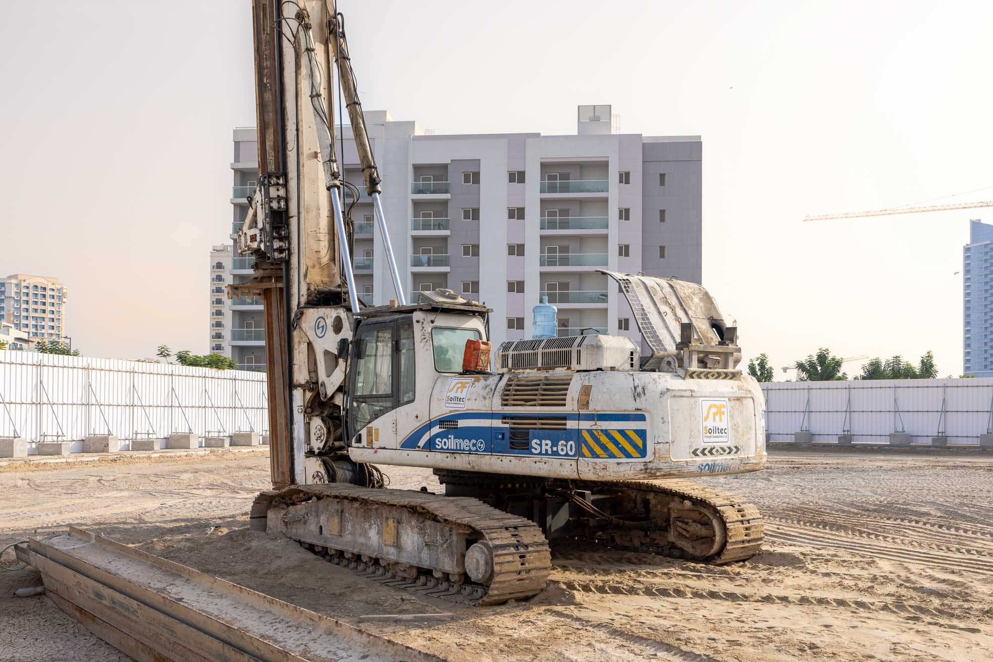 Cove Grand By Imtiaz A large construction machine, a Solitec SR-60, stands on a sandy site with buildings in the background.