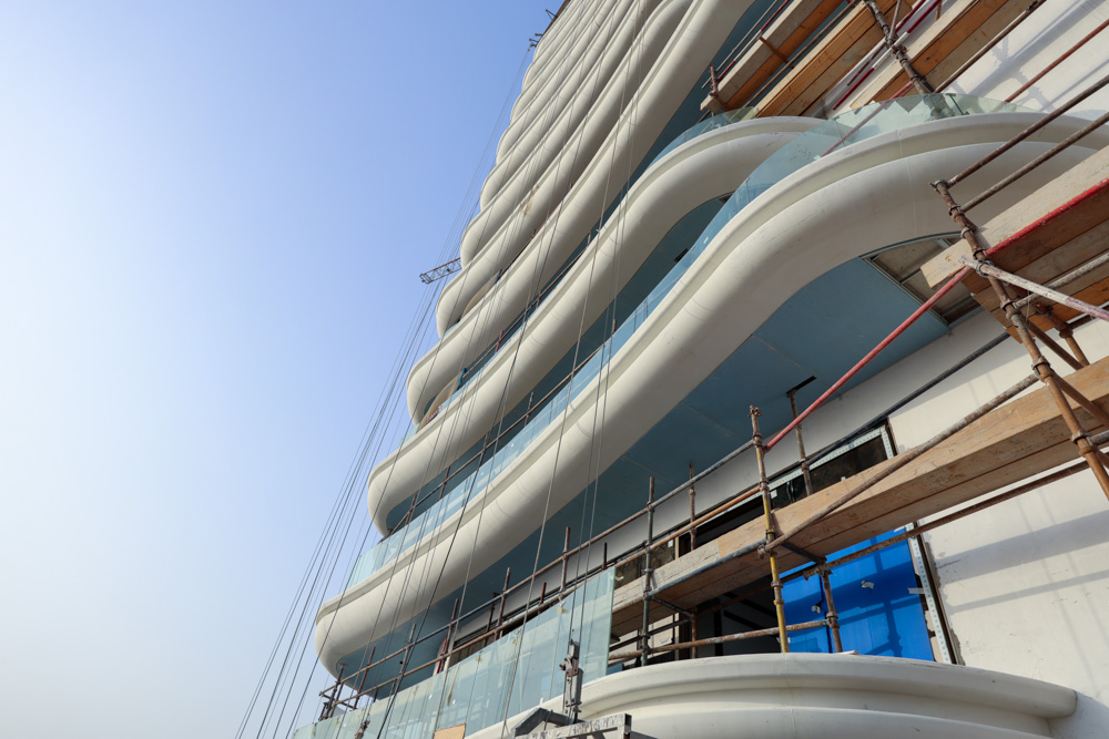 Beach Walk Residence An architectural view of a modern building under construction, featuring wavy balconies and scaffolding.