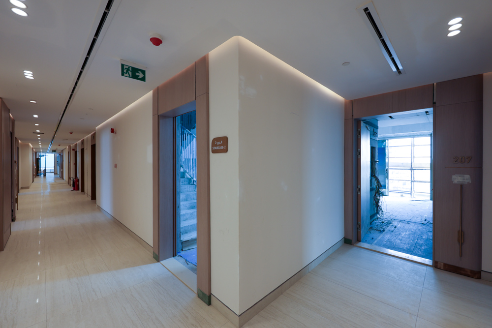 Beach Walk Residence A modern corridor with doors, one leading to an unfinished room and another to a staircase. Light and clean design.