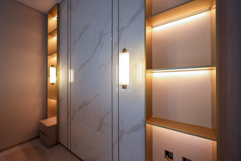 Beach Walk Residence A modern interior featuring light marble walls, stylish lighting, and a minimalist storage space.