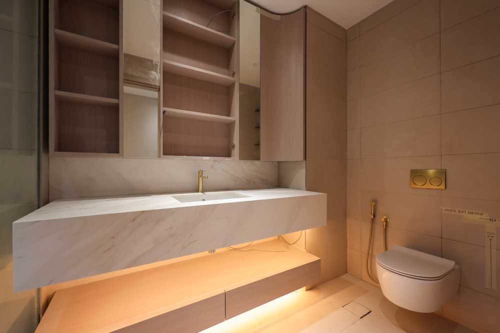 Beach Walk Residence A modern bathroom featuring a marble sink, wooden cabinetry, and a wall-mounted toilet with gold accents.