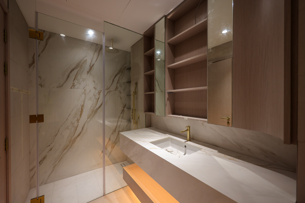 Beach Walk Residence A modern bathroom featuring a glass shower, marble accents, sleek vanity with gold fixtures, and wooden cabinetry.