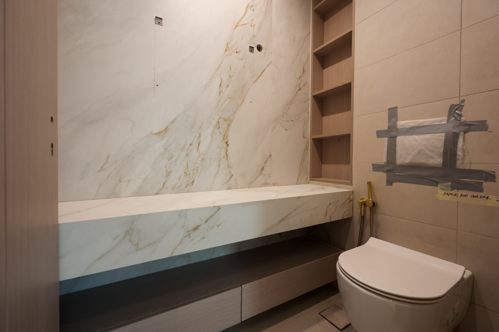 Beach Walk Residence Modern bathroom with marble walls, a sleek countertop, and a white toilet. Features storage shelving and unfinished details.