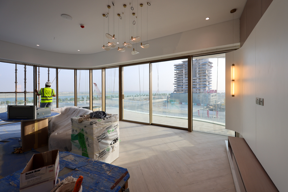Beach Walk Residence A worker in a safety vest stands in a modern room with large windows, overlooking a construction site and view.