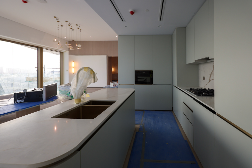 Beach Walk Residence A modern kitchen with light green cabinetry, a marble countertop, and unfinished elements, including a blue protective covering.